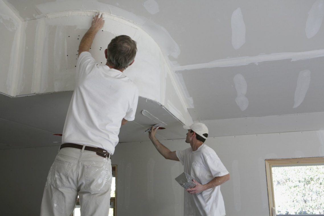 Deux hommes en train de peindre un plafond intérieur.