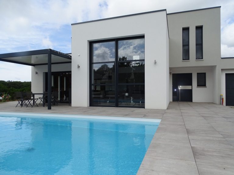 Maison moderne avec grande terrasse, piscine et grandes fenêtres, située dans un cadre paisible.